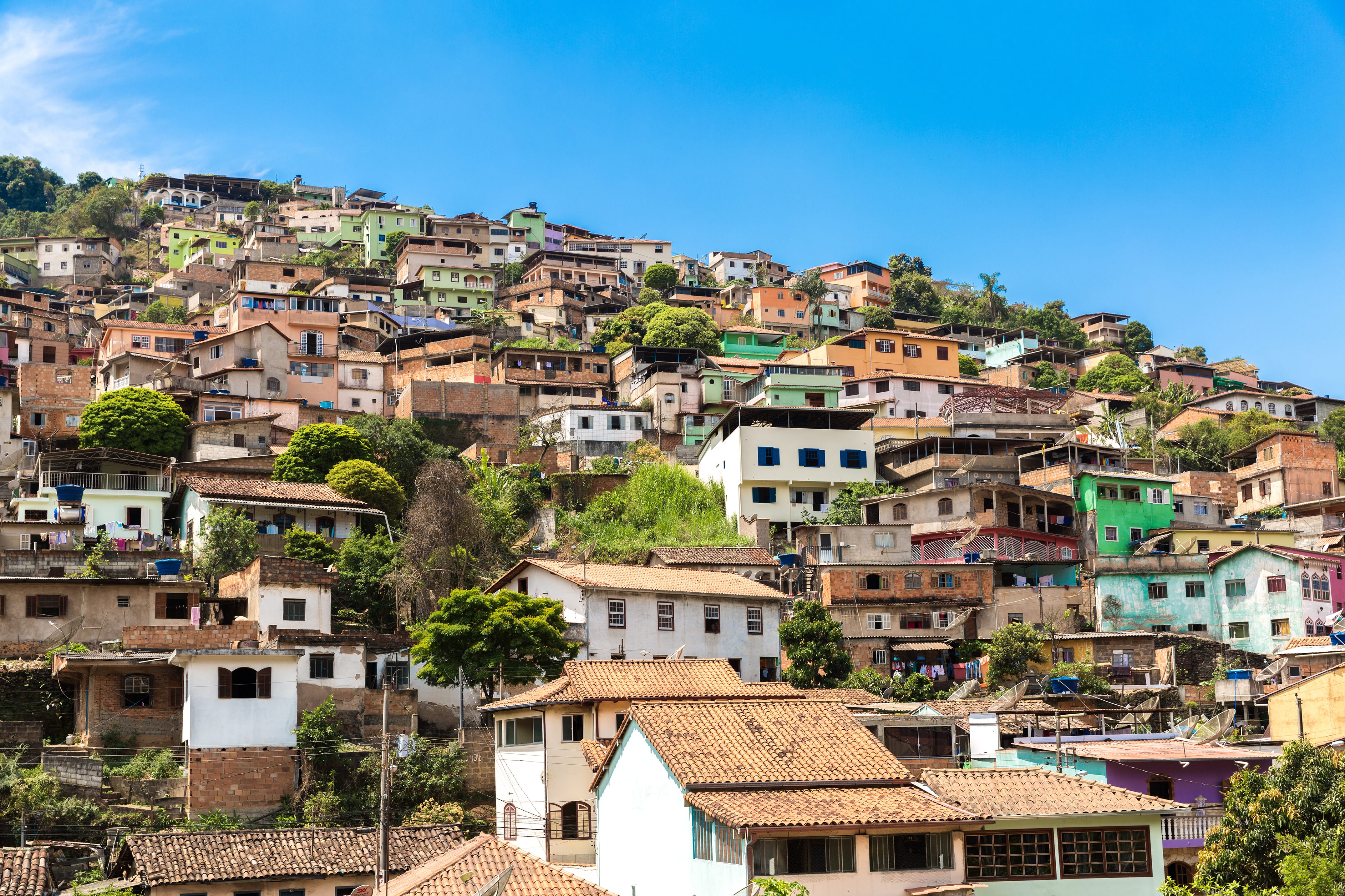 A imagem traz uma foto muito comum ao cenário brasieliro que são as favelas conhecidas mundialmente. O céu está limpo e bem azul. Na comunidade há um mix de cores entre as casas fazendo um lindo jogo de cor com predominância de tons marrons.
